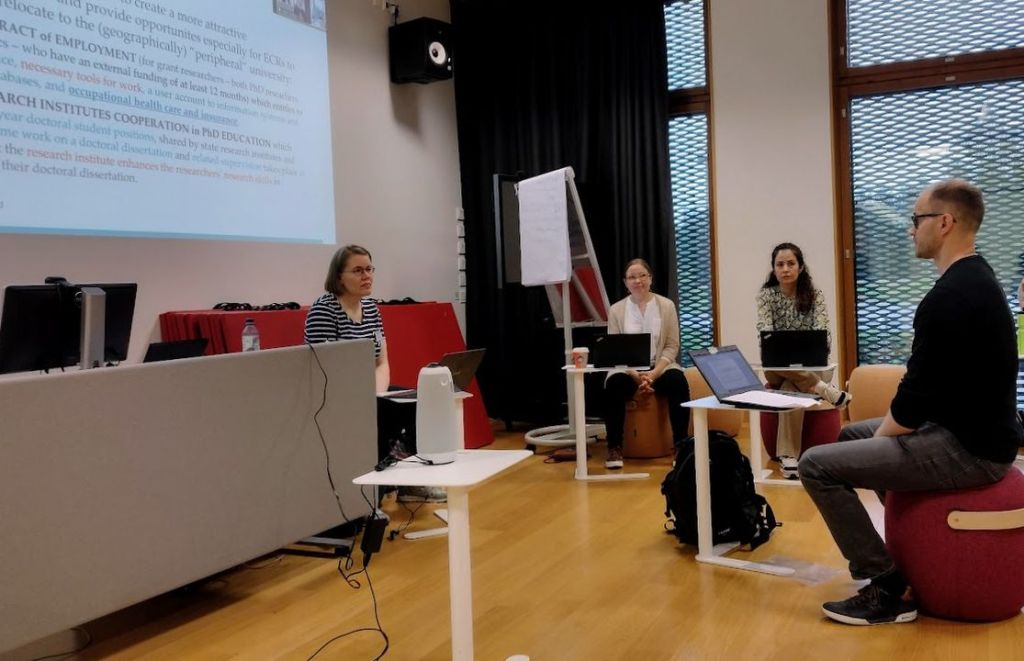 A group of four people are sitting in a circle in a lecture room.